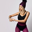 © Dmitry Lobanov - Portrait of stylish blonde woman in purple sport wear and winter hat standing looking at her smart watches setting