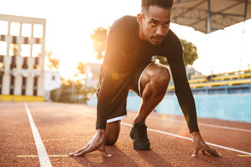 Image of african american man ready to start running on sports stadium