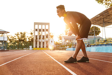 Sticker - Image of muscular african american man running on sports stadium