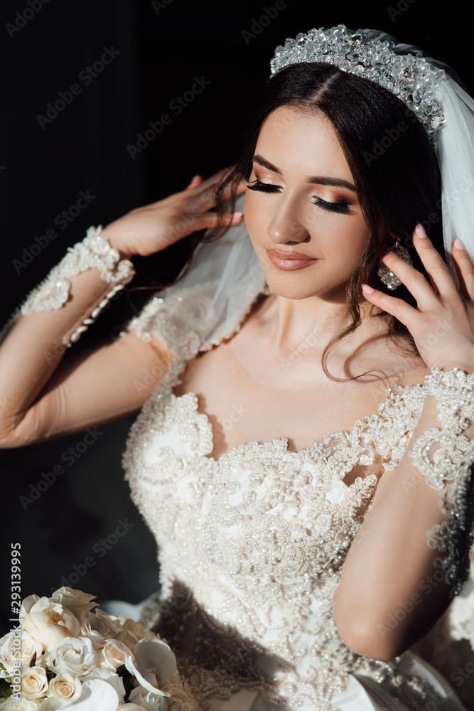 Fotografie Brunette bride in fashion white wedding dress. Female fashion.  Beautiful bride with closed makeup eyes and manicured nails. Fashion of  girl indoors. ve slub Stock | Adobe Stock