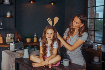 Beautiful young mother playing and having fun with her little cute daughter in a dark kitchen interior at home