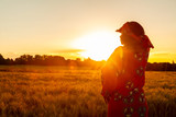 Fototapeta  - African woman in traditional clothes standing in a field of crops at sunset or sunrise