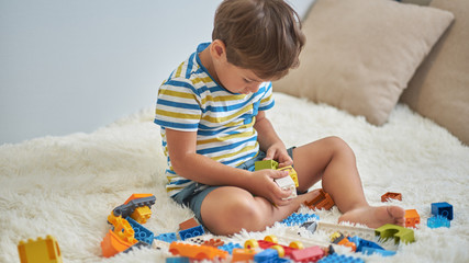 happy asian boy playing with colorful construction plastic blocks on white Bed at home.