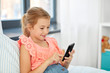 © Syda Productions - children, technology and communication concept - smiling girl using smartphone sitting on bed at home