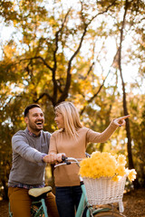 Wall Mural - Active young couple enjoying together in riding bicycle in golden autumn park