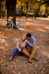 Wall Mural - Young couple sitting on ground in autumn park