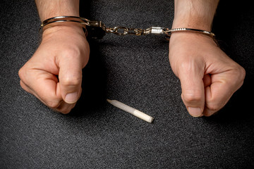 Man s hands in handcuffs and a cigarette with marijuana on a black background