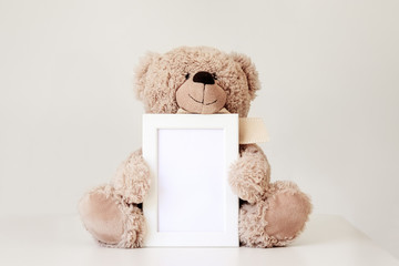 mockup. soft beige teddy bear toy holding white clean mock up frame with copy space sitting at light