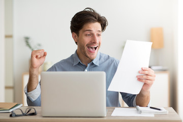 Canvas Print - Man Celebrating Victory Sitting At Laptop Holding Letter At Workplace