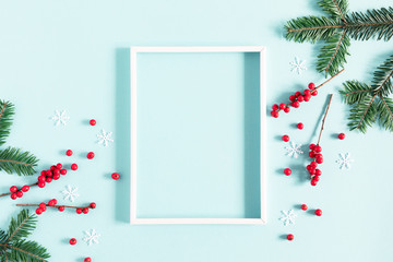Wall Mural - christmas holiday composition. photo frame, fir tree branches and red berries on pastel blue backgro