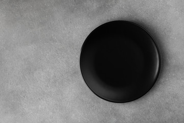 Black plate on gray stone table top view. Empty space for menu or recipe.