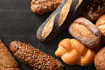 Poster - Mixed baguettes and bread rolls on dark grey wood. Top view. Space for text.