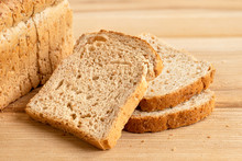 Three Slices Of Whole Wheat Toast Bread Isolated On Light Wood Next To A Loaf Of Bread.