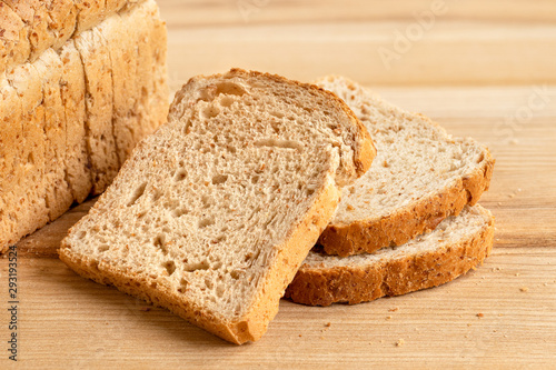 Fotografía Three slices of whole wheat toast bread isolated on light wood next to a loaf of bread