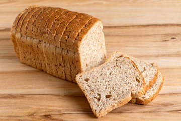 Wall Mural - Sliced loaf of whole wheat toast bread isolated on light wood. Three slices lying.