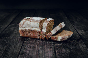 Healthy dark bread and sliced slices on a dark wooden background. The concept of baking bread, eating meals with rolls, bread. Product made of wheat and rye flour, bread preparation.