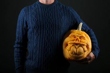 Wall Mural - Studio shot of young man wearing blue knitted sweater with jack o lantern. Portrait of hipster male holding halloween pumpking by his side. Background, close up, copy space, isolated.