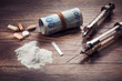 Vintage syringes, cocaine, pills and rolled dollar bills on wooden table