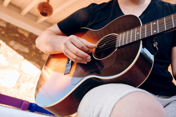 Hands of a young male playing acoustic guitar in the garden