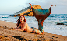 Caucasian Redhead Woman With Mermaid Tail Reclines On The Beach In The Waves
