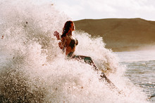 Caucasian Redhead Woman With Mermaid Tail Perches On Rock With Pounding Waves Around Her