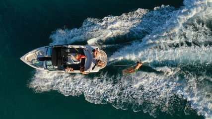 Wall Mural - Aerial photo of woman practising waterski in Mediterranean bay with emerald sea at sunset