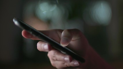 Gadget technology or communication concept : Close up woman hands using smart phone in dark room in front of computer monitor.