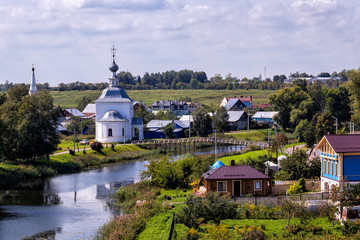 Idyllic Russian summer rural landscape with apartment buildings, church, river. Suzdal vastness, Russia.