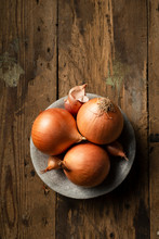 Brown Onions And Shallots In A Stone Bowl, On A Rustic Timber Background.
