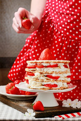 Sticker - Woman decorating strawberry layer cake with fresh fruits.