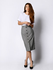 Wall Mural - Young beautiful woman posing in new white bluesque and gray skirt on high heels full body on a white background