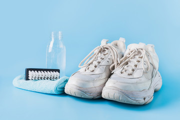 Dirty white sneakers with special tool for cleaning them on blue.