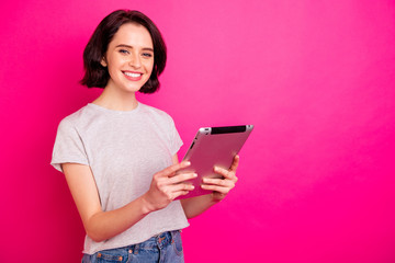 Portrait of cheerful excited freelancer using tablet searching news wearing white t-shirt isolated over pink fuchsia background