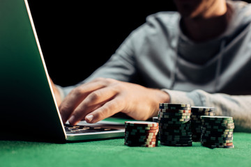 cropped view of man typing on laptop near poker chips isolated on black