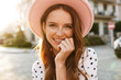 © Drobot Dean - Redhead woman walking by street outdoors in dress and hat.
