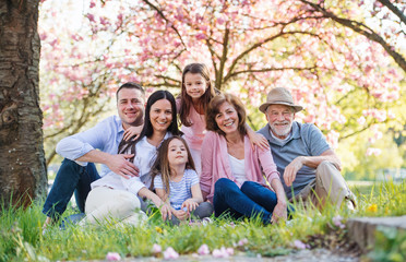 Three generation family sitting outside in spring nature, looking at camera.