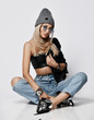 © Dmitry Lobanov - Young grunge style girl in torn blue jeans, leather bralet, chrome boots and winter hat sitting cross-legged on floor