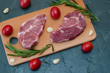 Flat lay, raw meat two pork steak with tomatoes garlic and rosemary on a wooden cutting board close-up