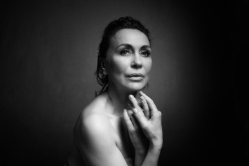 Portrait of a sensual fifty year old woman on grey studio background. Monochrome shot.