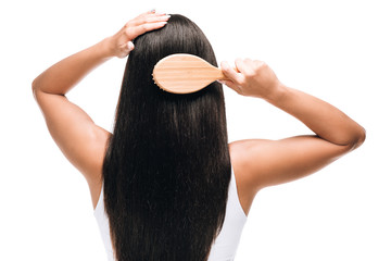 back view of brunette beautiful woman brushing long straight healthy and shiny hair with comb isolated on white