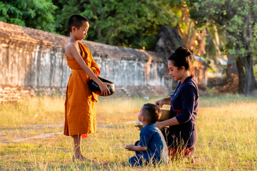 Buddhist elder Novice. The family Children woman putting food offerings in a monk's alms bowl and a woman prostrating oneself to respect worship monks, monks walking routine every morning.