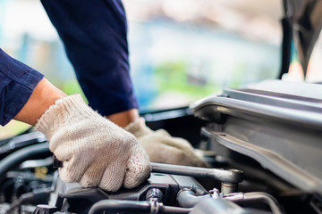 Close up, Asian man auto mechanic using a wrench and screwdriver to working service car in garage.