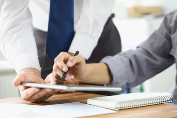 Two businessman are looking and studying statistics on tablet display closeup. Male hand opponent holds pen and points out problem collaboration business coach partnership digital sign concept