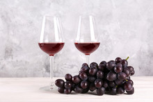 Two Glasses Of Vintage Red Wine And Bunch Of Grapes On Wooden Table, Grunged Concrete Wall Background. Expensive Bottle Of Cabernet Sauvignon Concept. Copy Space,