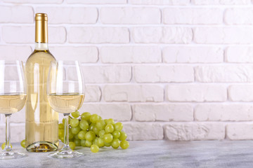 Vintage bottle of white wine without label, two glasses and bunch of grapes on wooden table, lofty white brick wall background. Expensive bottle of chardonnay concept. concept. Copy space.