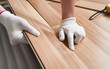 © Lubo Ivanko - Installing laminated floor, detail on man hands in white gloves positioning wooden tile, over white foam base layer