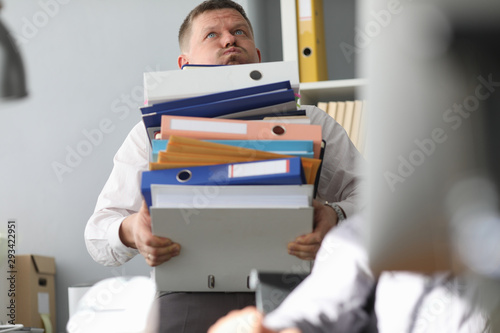 Cuadros en Lienzo Male businessman carries a bunch of folders and documents in hand against office background