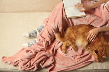 Poster - Woman with cute red cat and book on sofa at home, closeup view. Space for text