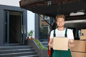 Canvas Print - Young courier with parcel near delivery car outdoors. Space for text