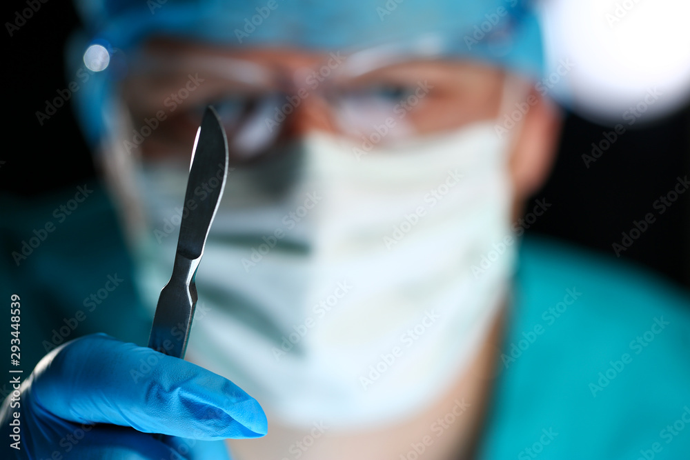 Operating Human Using Razor Knife Surgeon arms in sterile uniform holding sharp knife while operating ...